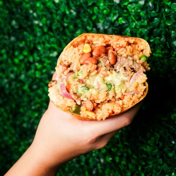 A hand holds a Big Papi's burrito, cut in half, revealing rice, beans, meat, and guacamole.
