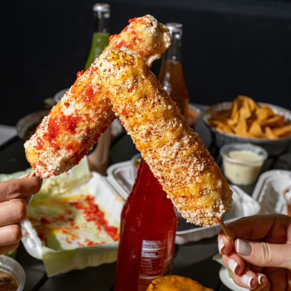 Two hands holding Big Papi's elotes, Mexican street corn, topped with cheese and chili powder.
