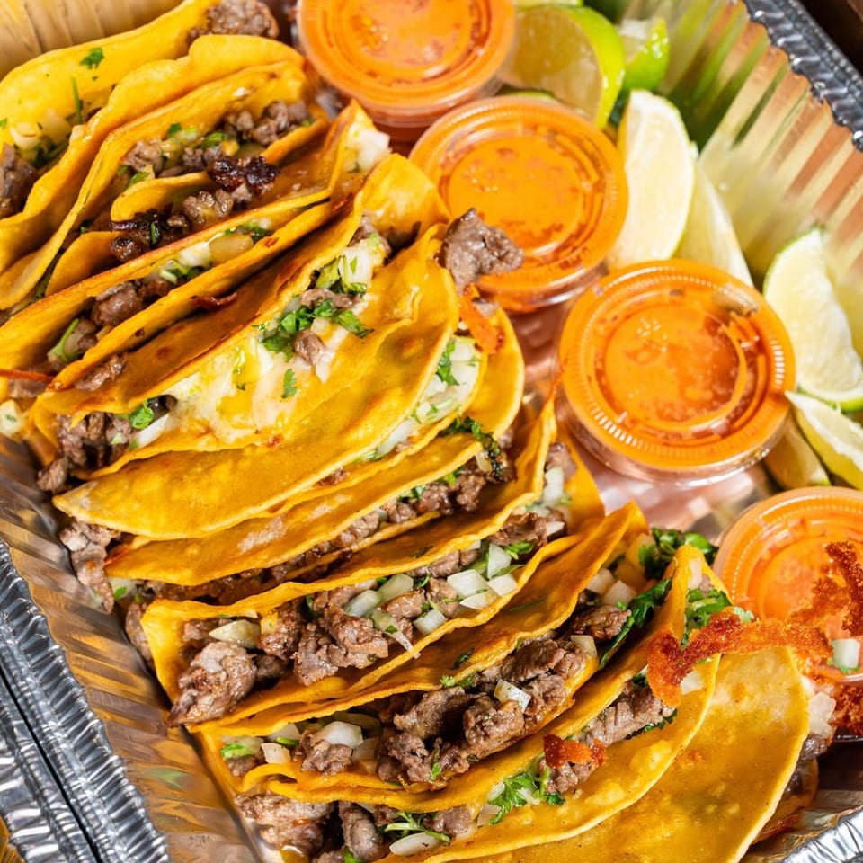 Big Papi's beef tacos with cilantro, onions, lime wedges, and salsa in a foil tray.
