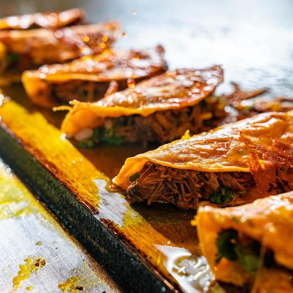 Close-up of several Big Papi's birria tacos sizzling on a griddle, filled with meat and cilantro.
