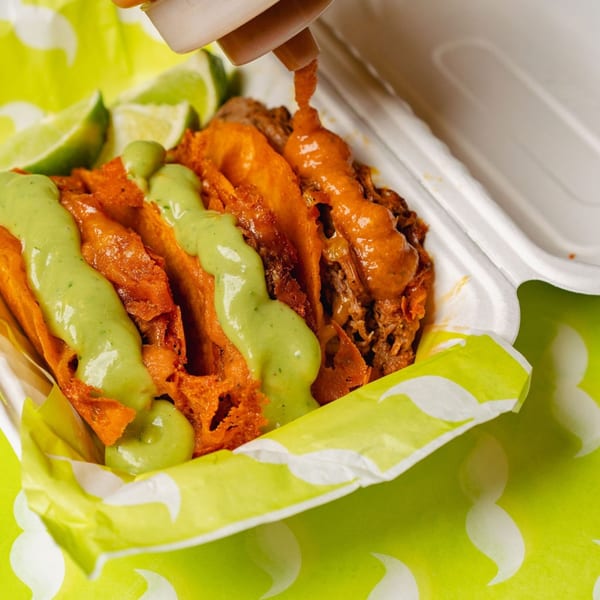 Big Papi's birria tacos with green and red sauce, and lime wedges in a takeout container.