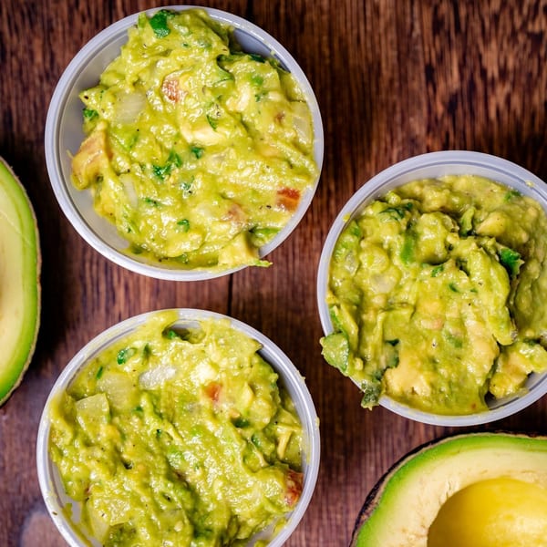 Three cups of Big Papi's guacamole with avocado halves on a wooden table.